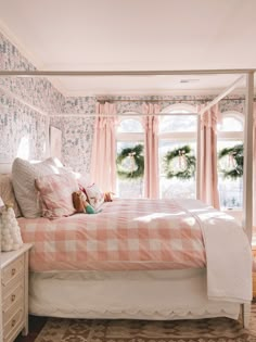 a bedroom with pink and white bedding, wreaths on the windows