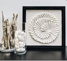 two glass vases with seashells in them on a table next to a framed artwork