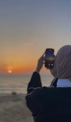 a woman taking a photo with her cell phone on the beach at sunset or sunrise