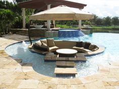 an outdoor living area with couches, umbrellas and water feature in the pool