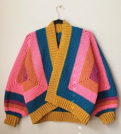 a colorful knitted sweater hanging on a white wall next to a coat hanger