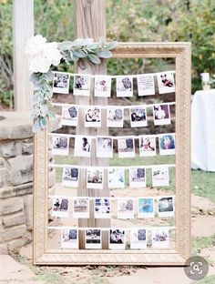 a wooden frame with photos hanging from it and flowers on the top is next to a tree