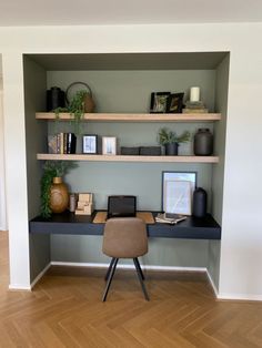 a desk with a laptop and some books on top of it in front of a wall