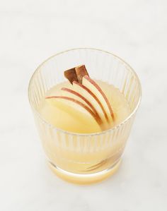 an apple dessert in a glass bowl on a white counter top with some cinnamon sticks sticking out of it