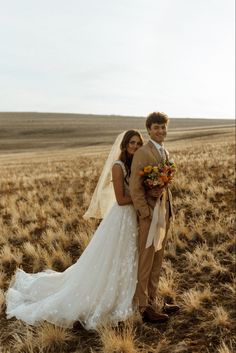 a bride and groom standing in the middle of an open field with tall dry grass