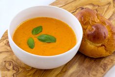 a bowl of soup next to a roll on a cutting board with a green leafy garnish