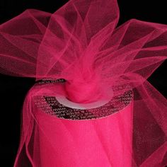 a roll of pink tulle sitting on top of a black surface with a ribbon around it