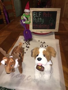 two stuffed dogs sitting on top of a table next to a sign that says elf potty training