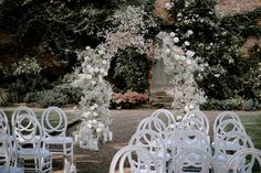 an outdoor wedding setup with white chairs and flowers on the arch in front of it