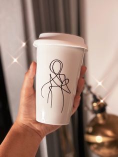 a hand holding a coffee cup with a drawing on it