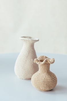 two white crocheted vases sitting on top of a blue table cloth covered surface