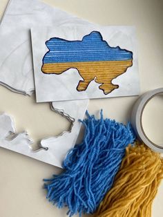 two pieces of paper with the shape of ukraine on them next to scissors and yarn