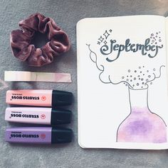 an open notebook with markers, pens and a scrunchy bun