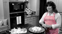 a woman in an apron standing next to a plate with cupcakes on it