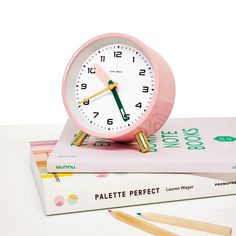 a pink alarm clock sitting on top of two books and pencils next to it