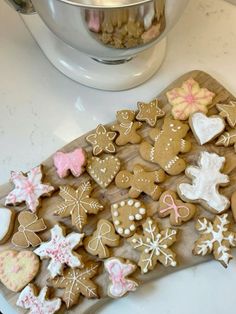 a wooden cutting board topped with lots of cut up cookies next to a metal bowl