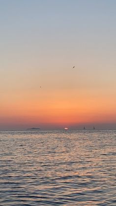 the sun is setting over the ocean with sailboats in the distance