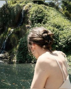 a woman standing in front of a waterfall with her back turned to the camera,