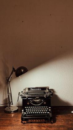 an old fashioned typewriter sitting on top of a wooden table next to a lamp