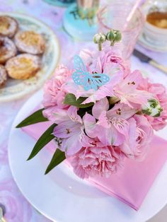 pink flowers in a vase on a table with other plates and desserts behind it