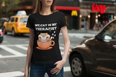 a woman is standing on the street with her hands in her pockets while wearing a t - shirt that says, my cat is my therapisst