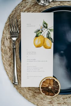 a place setting with two lemons on it and a menu card next to the plate