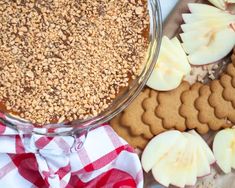 an apple pie is surrounded by cookies, apples and crackers on a tablecloth