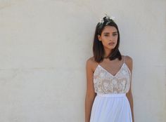 a woman wearing a white dress standing next to a wall with flowers in her hair