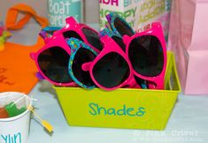 pink and blue sunglasses sitting in a green box next to a cup with candy on it