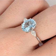 a woman's hand wearing a ring with an aqua blue topazte and diamond accents