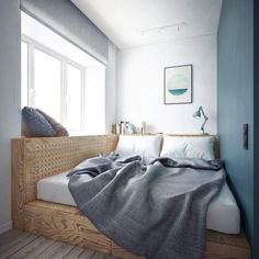 a bed sitting under a window next to a wooden shelf filled with pillows and blankets