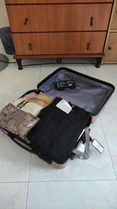 an open suitcase on the floor with clothes and other items in it next to a dresser