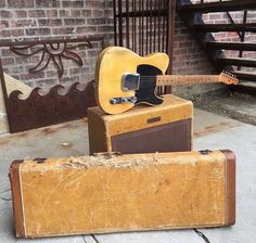 an old suitcase and guitar sit on the sidewalk