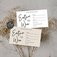 two business cards sitting on top of each other next to some dried plants and flowers