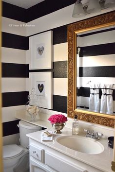 a bathroom decorated in black and white with striped walls, gold framed mirror over the toilet