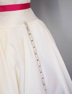 a white dress with a measuring tape on it's back and pink sash around the waist