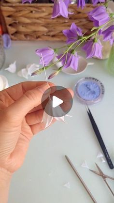 a person is holding some scissors and purple flowers in front of the camera, next to other crafting supplies