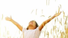 a woman standing in tall grass with her arms spread out to catch the sun's rays