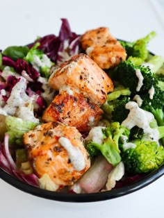 a salad with shrimp, broccoli and dressing in a black bowl on a white table