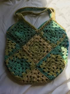 a crocheted purse sitting on top of a white bed next to a pillow