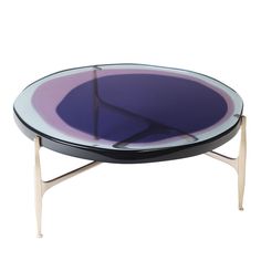 an oval glass table with metal legs and a purple center piece on the top, against a white background