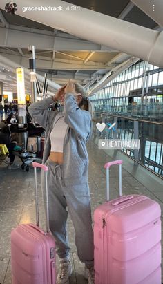 a woman standing next to two pink suitcases in an airport terminal with her hands on her head