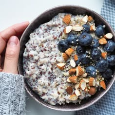 a bowl of oatmeal with blueberries and almonds in someone's hand