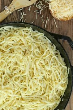 a skillet filled with pasta and cheese on top of a wooden table next to a spatula