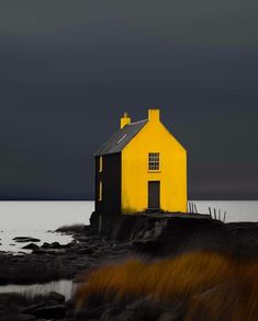 a yellow and black house sitting on top of a rocky beach next to the ocean