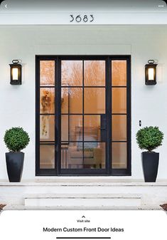 two large black vases with plants in them on the side of a white house