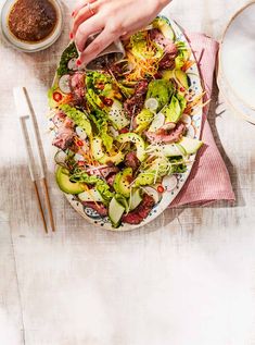 a person is cutting into a salad on a plate with chopsticks next to it