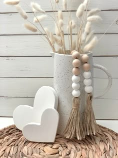 a white mug with some tassels and a heart on the table next to it