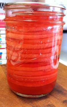 a jar filled with red liquid sitting on top of a wooden table next to books