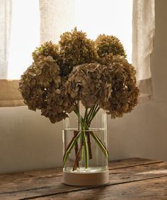 a vase filled with lots of flowers on top of a wooden table next to a window